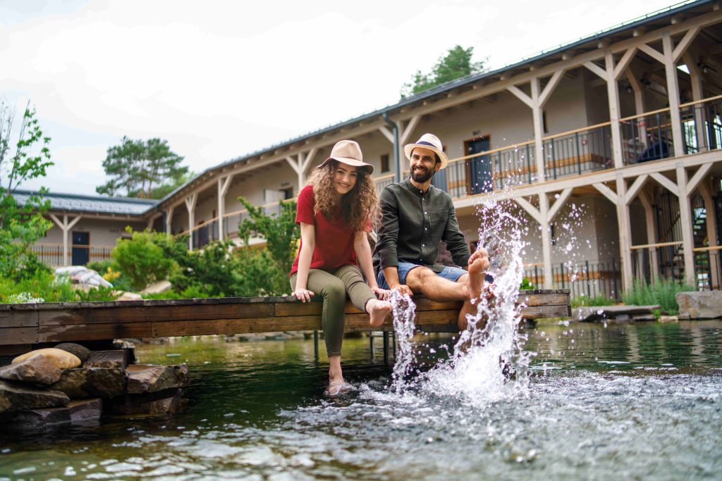 young-couple-sitting-outdoors-by-lake-hotel-on-hol